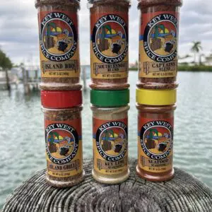 Six colorful spice jars labeled 'Tropical Isle' arranged on a wooden surface near water.
